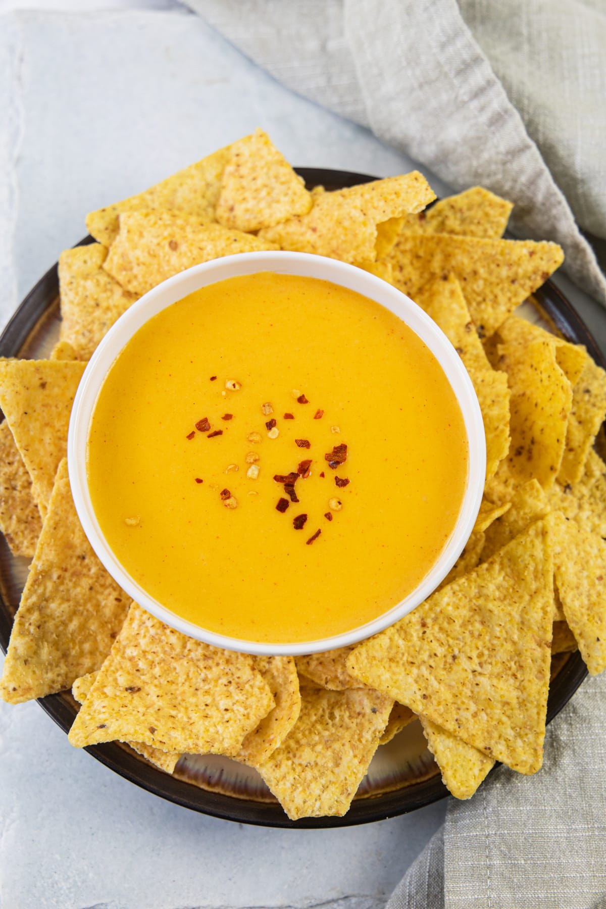 Nacho cheese sauce garnished with chili flakes and served with nacho chips.