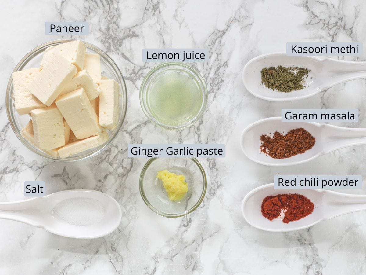 Paneer marination ingredients for paneer pakora in spoons and bowls with labels.