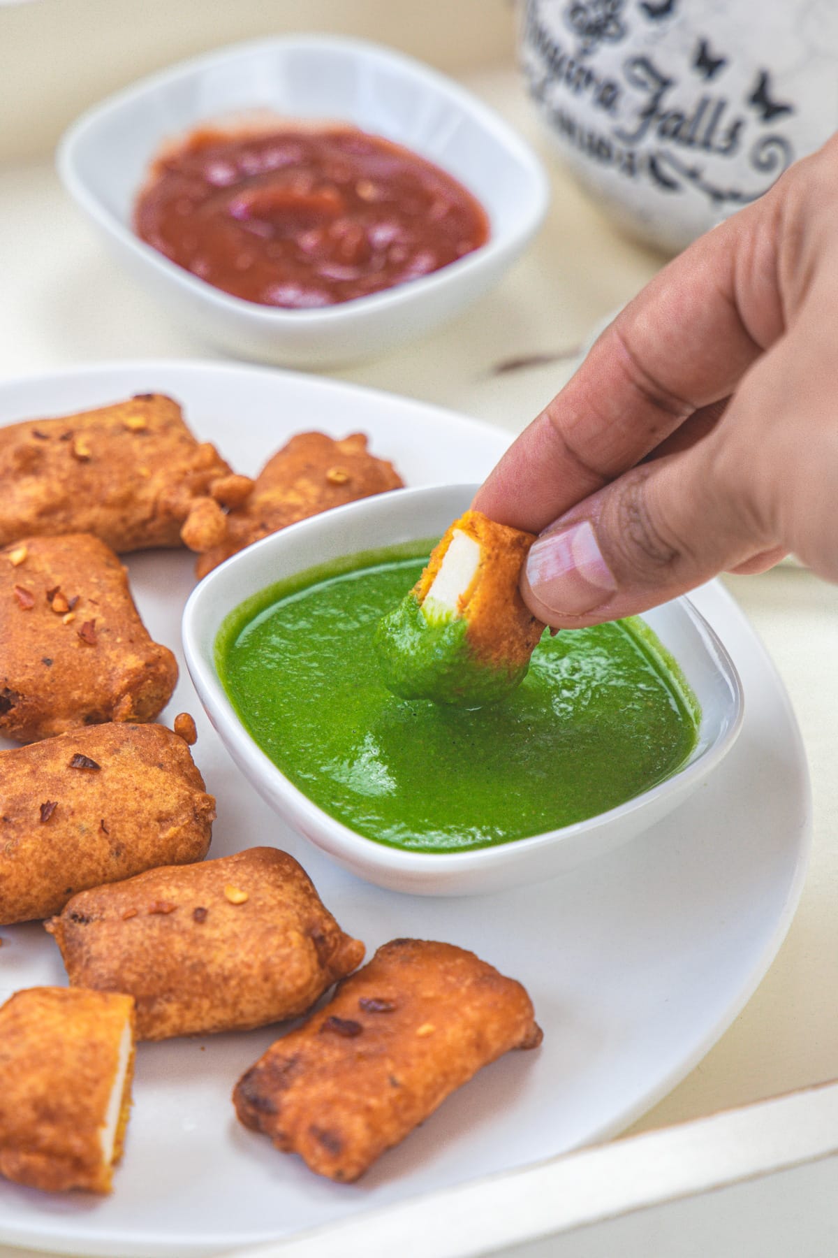 A piece of paneer pakora dipped into green chutney.