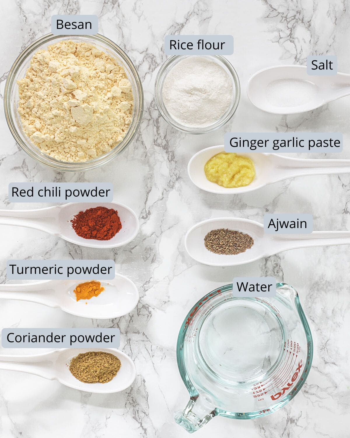 Paneer pakora batter ingredients in bowls and spoons with labels.