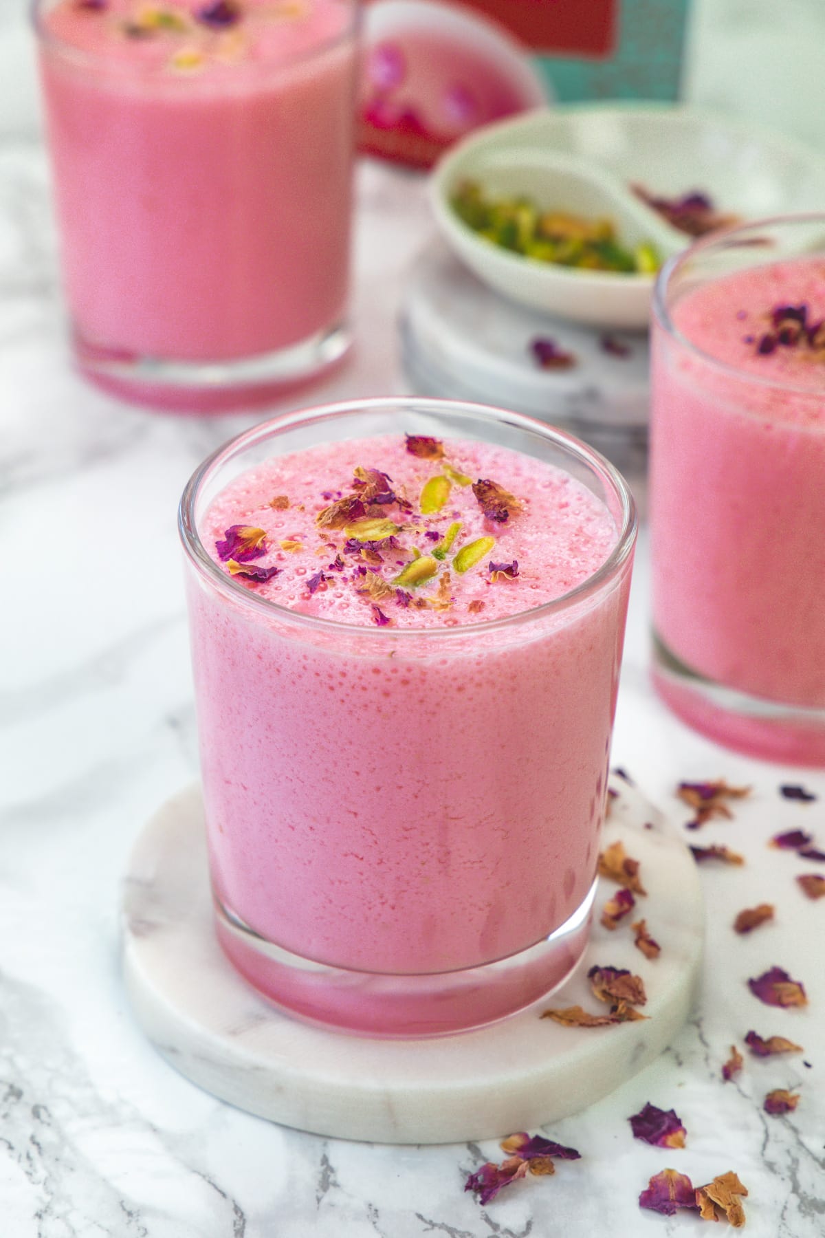 3 glasses of rose lassi with rose petals on the side.