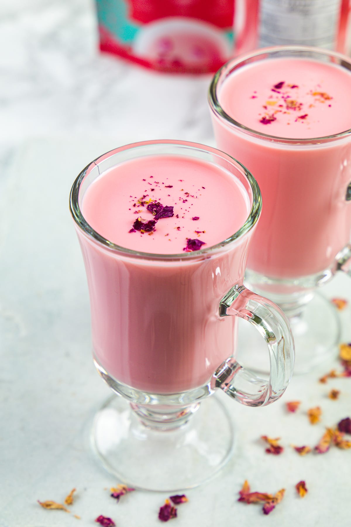 Rose milk served in 2 glasses garnished with rose petals.