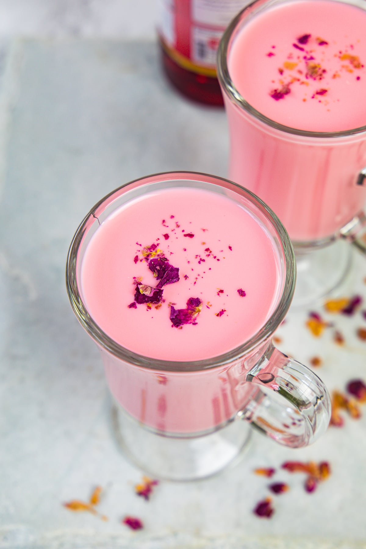 2 glasses of rose milk garnished with rose petals and few more petals on the side.