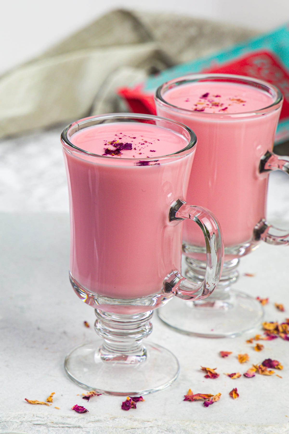 2 glasses of rose milk with napkin and rose petal packet in the back.