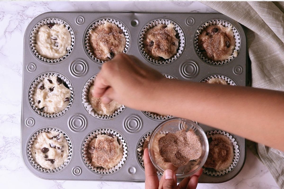 Sprinkling cinnamon sugar on the muffin batter.