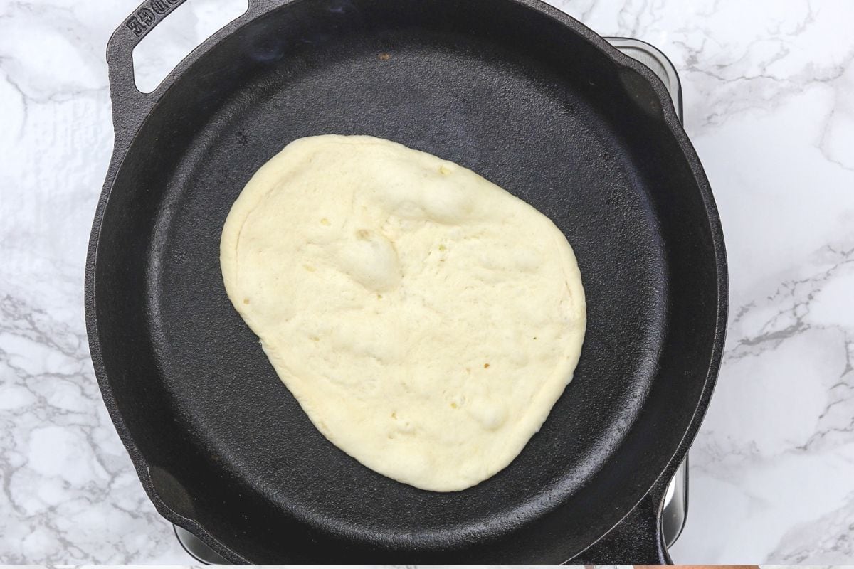 Cooking garlic naan in a cast iron skillet.