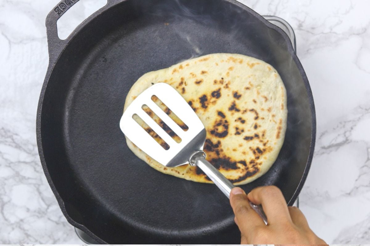 Cooking another side of garlic naan by pressing with spatula.