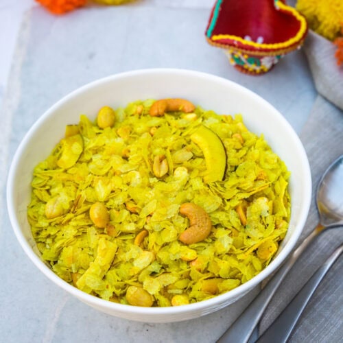 A bowl of roasted poha chivda with spoons on the side and diya in the back.