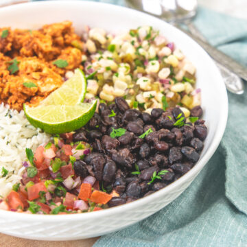 A burrito bowl with black beans, salsa, corn salsa, rice and limes.