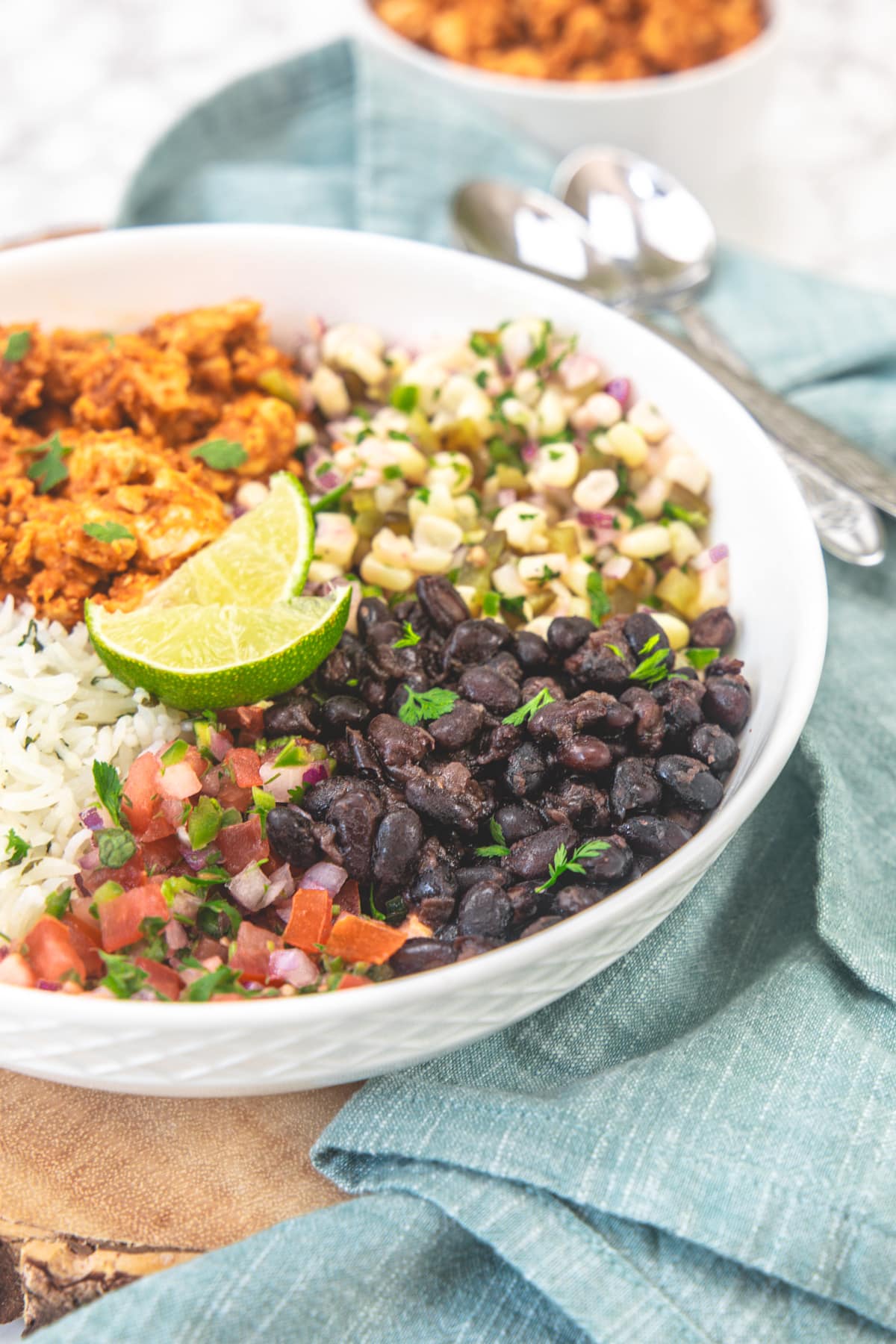 A burrito bowl with black beans, salsa, corn salsa, rice and limes.