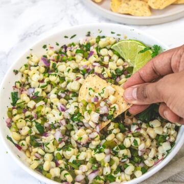 Scooping roasted chili corn salsa with a tortilla chip.