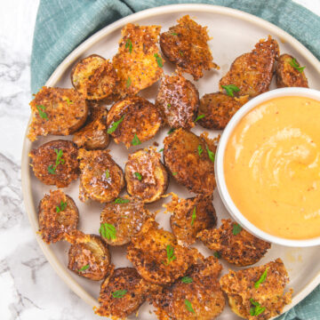 Parmesan crusted potatoes in a plate with a bowl of dipping sauce.