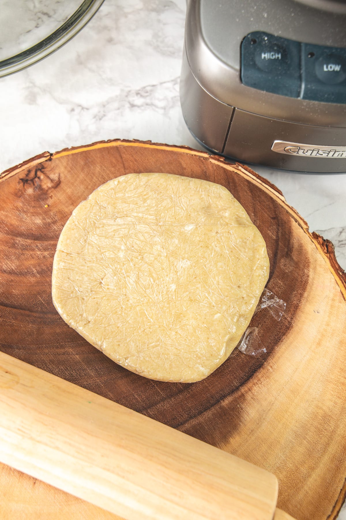 Pie dough wrapped in plastic wrap on a wooden board.