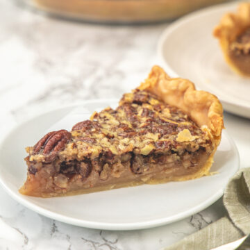 A slice of eggless pecan pie in a plate with fork and pie plate in the back.