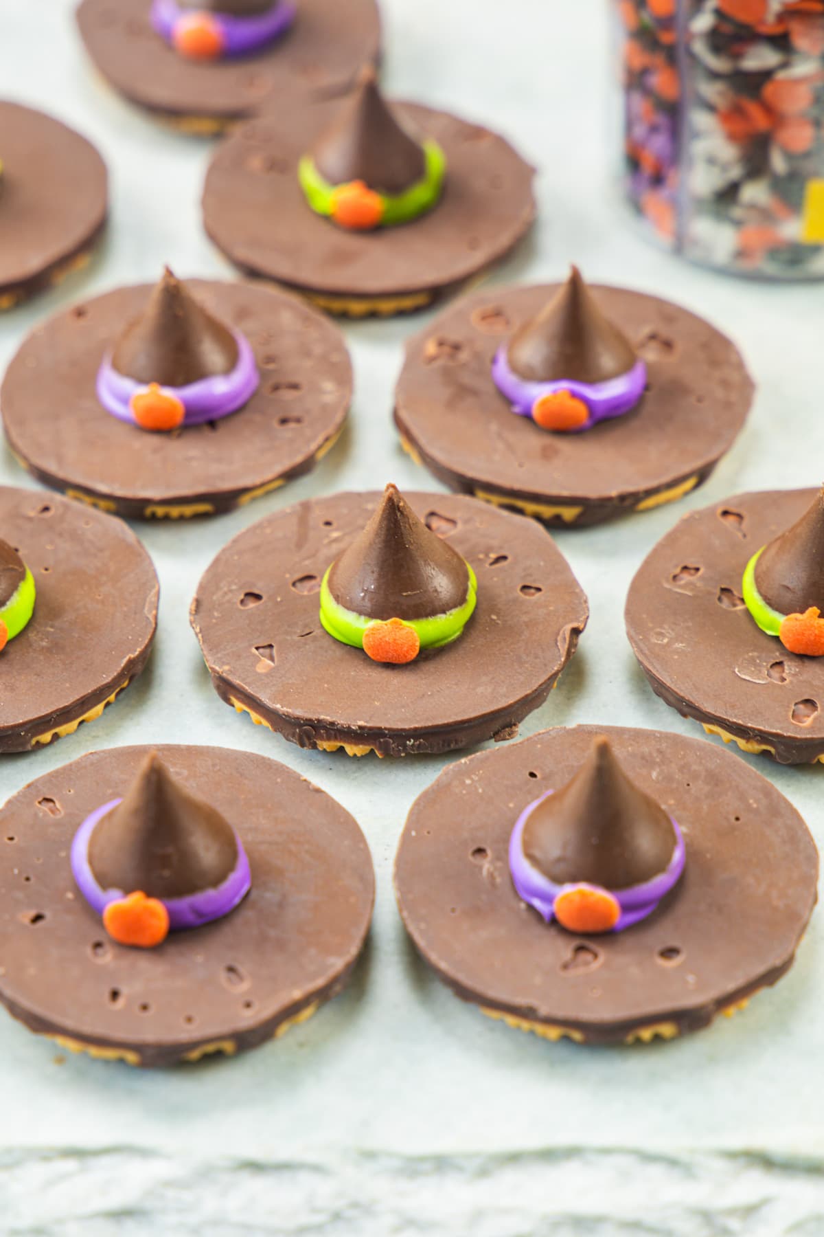 Witch hat cookies on a marble board with sprinkles container in the back.