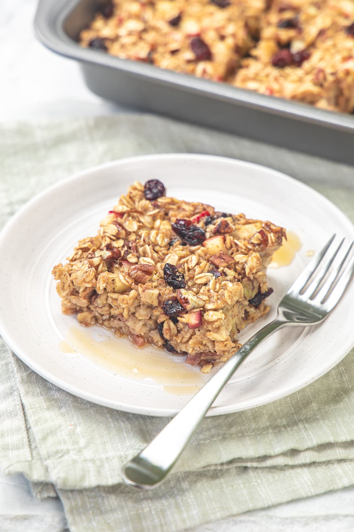 Apple baked oatmeal served in a plate with fork and a drizzle of maple syrup.