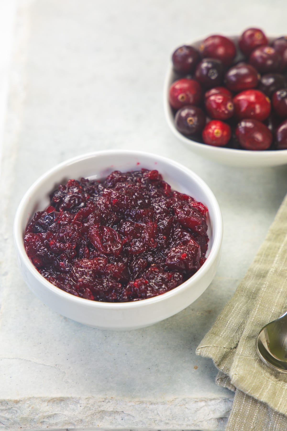 A bowl of cranberry chutney with a bowlful of cranberries in the back.