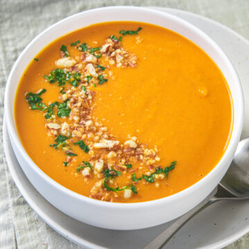 A bowl of curried pumpkin soup garnished with cilantro and crushed peanuts.