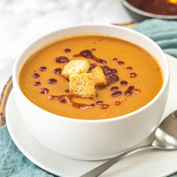 A bowl of red lentil soup with a drizzle of chili oil and garnished with croutons.