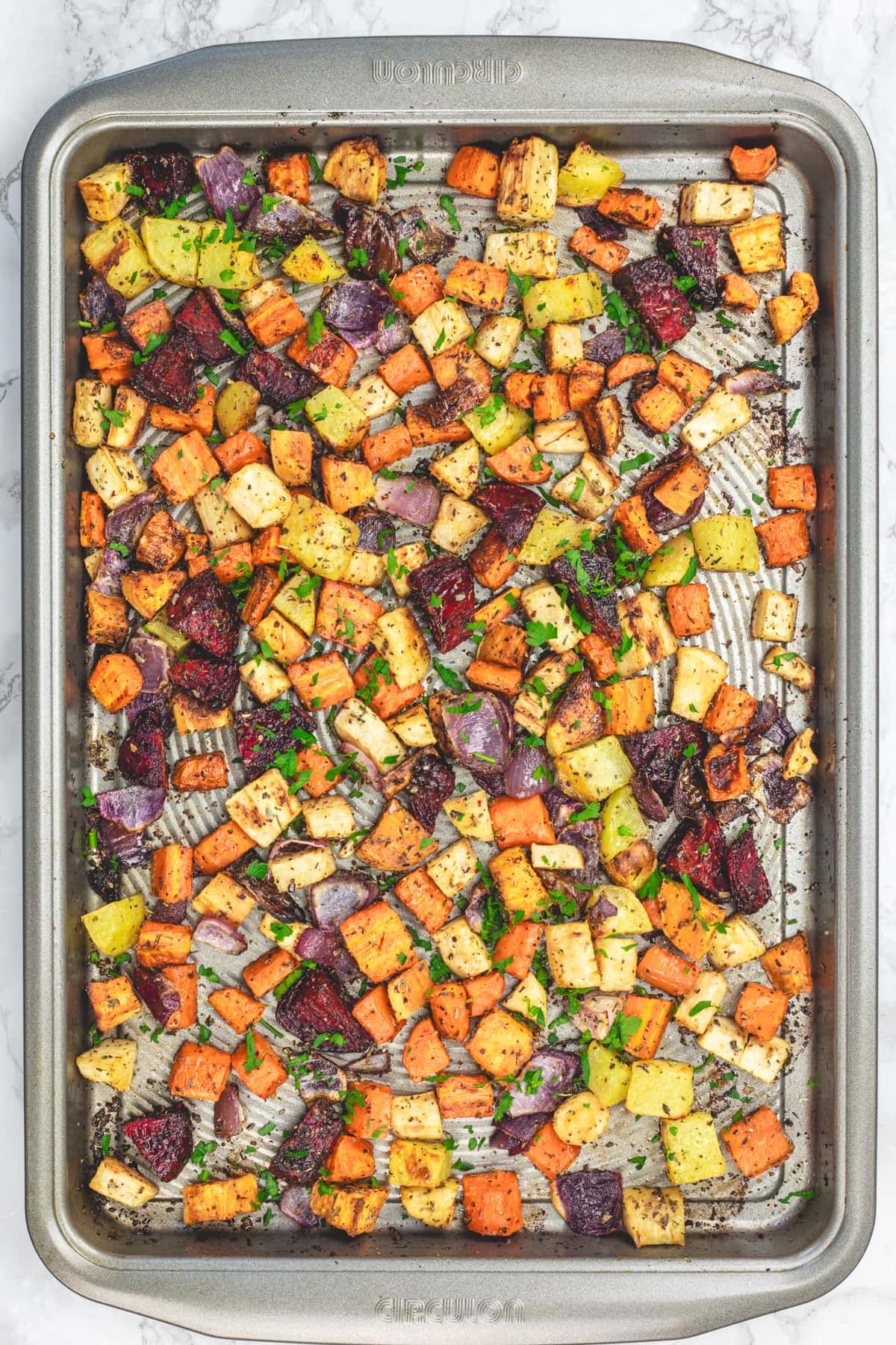 Roasted root vegetables in a baking tray garnished with fresh parsley.