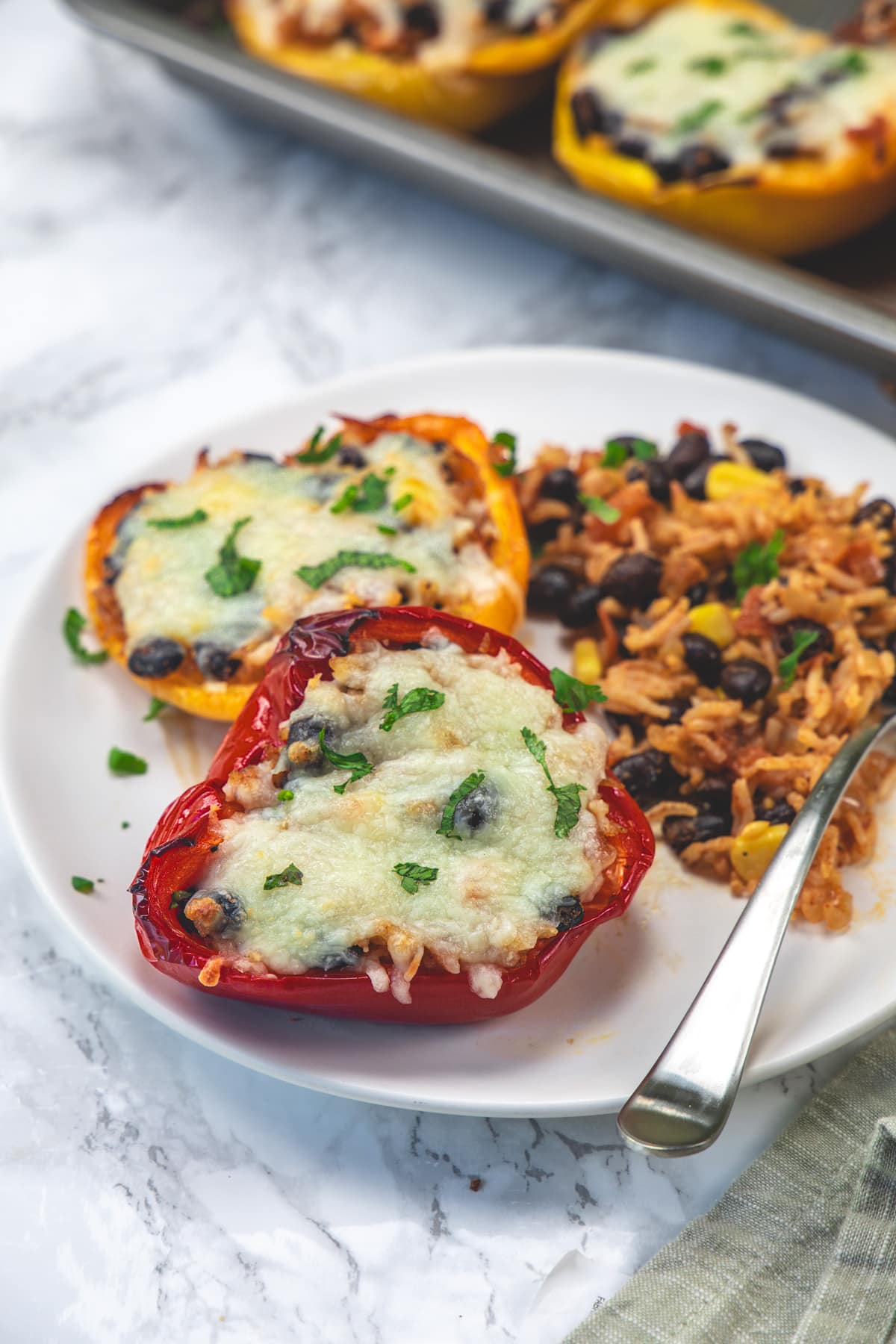 2 vegetarian stuffed peppers served in a plate with extra stuffing on the side.