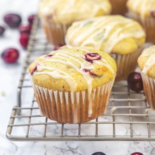 Eggless cranberry orange muffins on a wire rack with a few fresh cranberries scattered around.