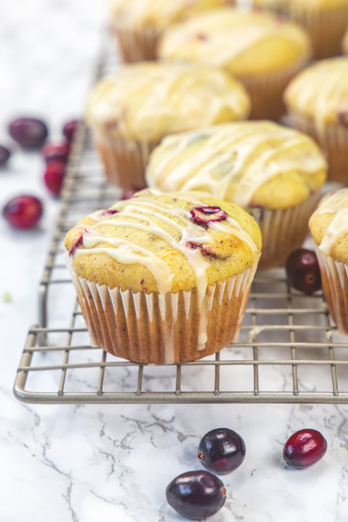 Eggless cranberry orange muffins on a wire rack with a few fresh cranberries scattered around.