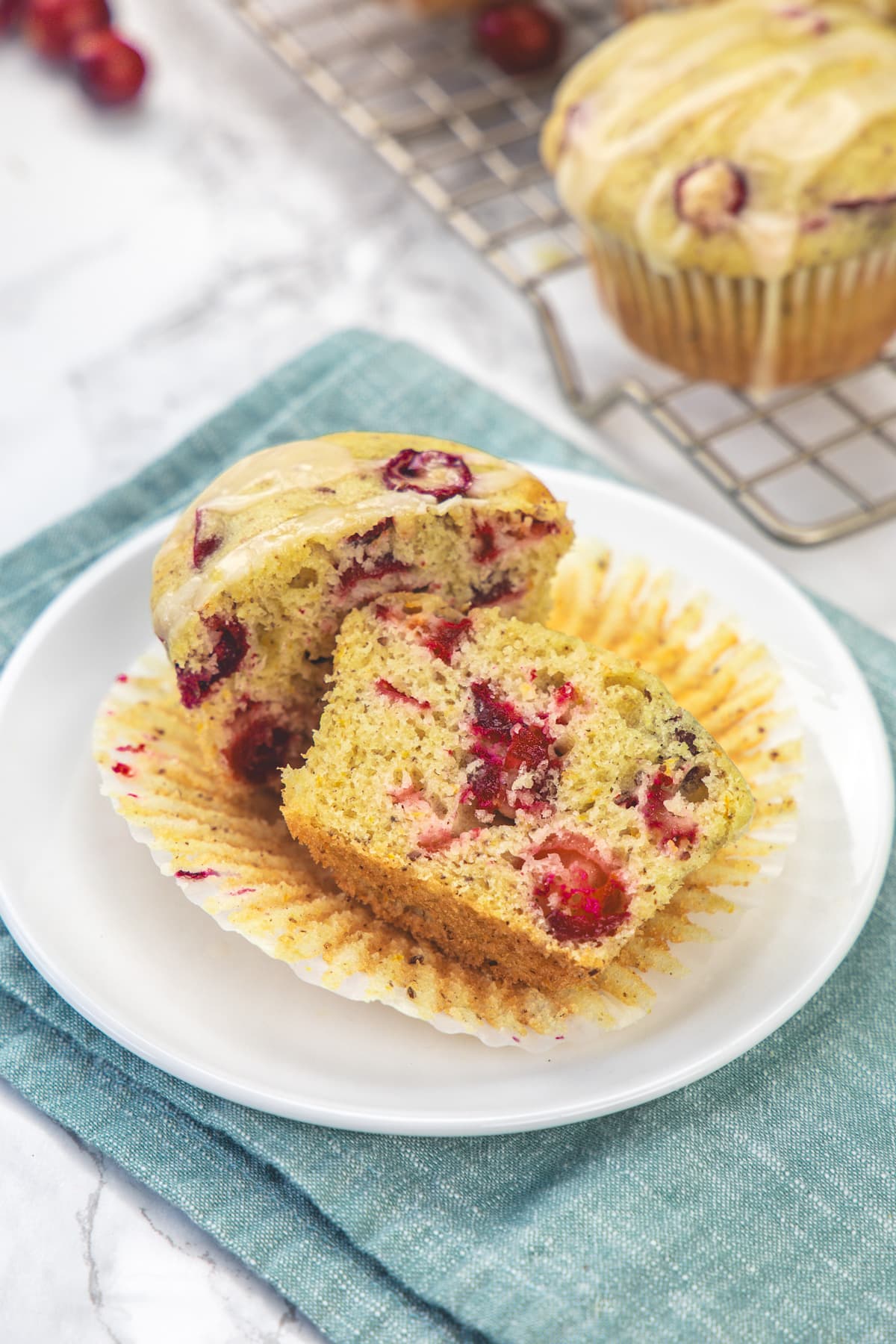 Eggless cranberry orange muffin cut into half in a small plate with napkin under the plate.