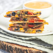 A stack on black bean quesadillas in a plate with napkin and wooden board under the plate.