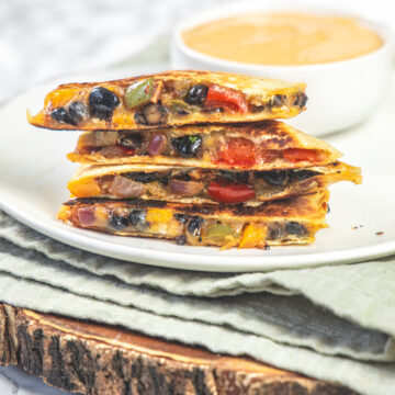 A stack on black bean quesadillas in a plate with napkin and wooden board under the plate.