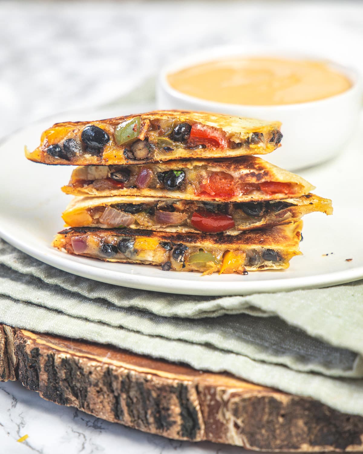 A stack on black bean quesadillas in a plate with napkin and wooden board under the plate.