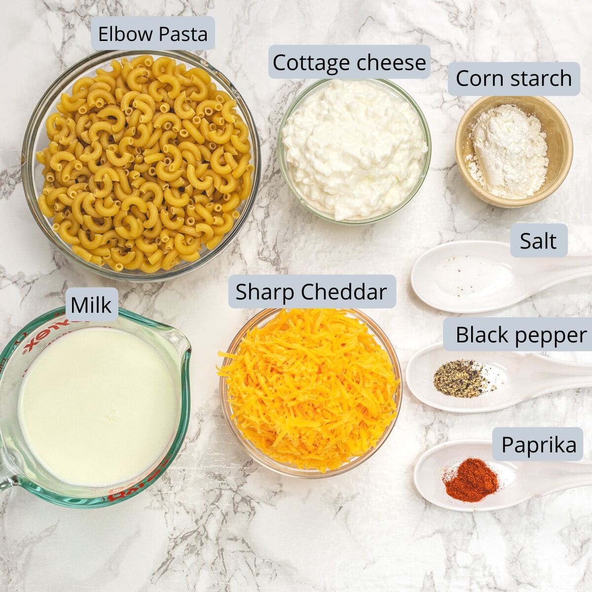 Ingredients for cottage cheese mac n cheese in bowls and spoons with labels.