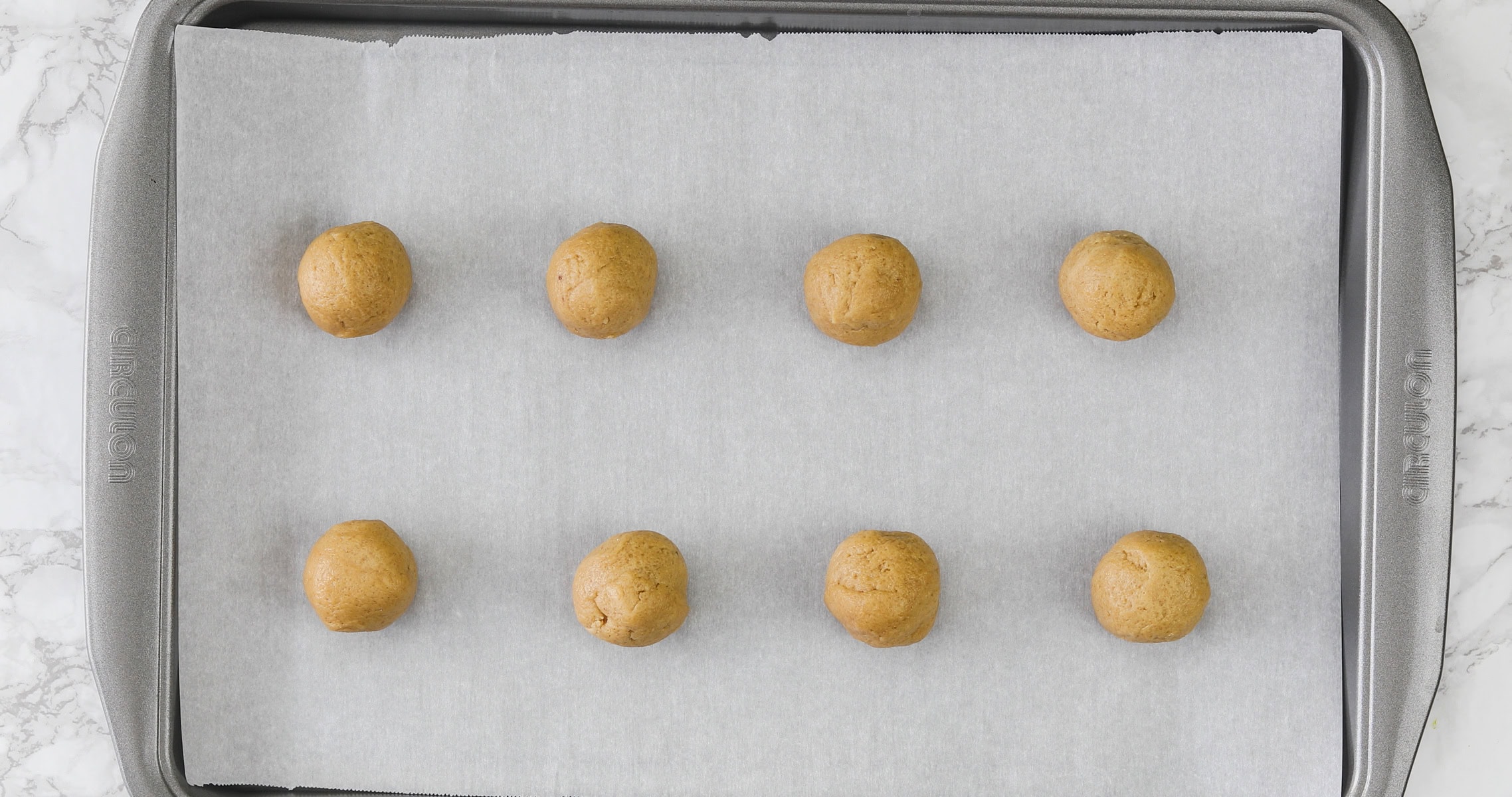 Eggless peanut butter cookie dough balls arranged on a cookie sheet.