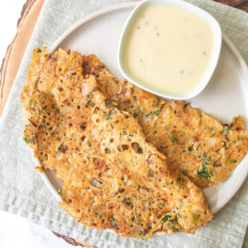 2 jowar dosa with coconut chutney in a plate with napkin and wooden board under it.