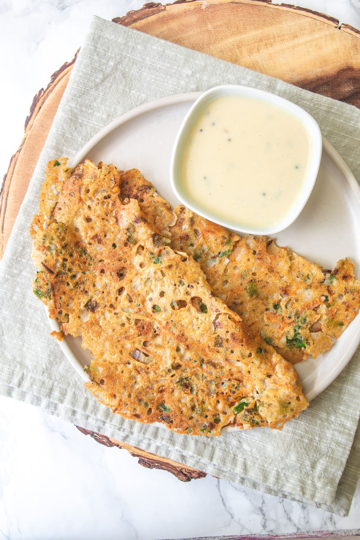 2 jowar dosa with coconut chutney in a plate with napkin and wooden board under it.