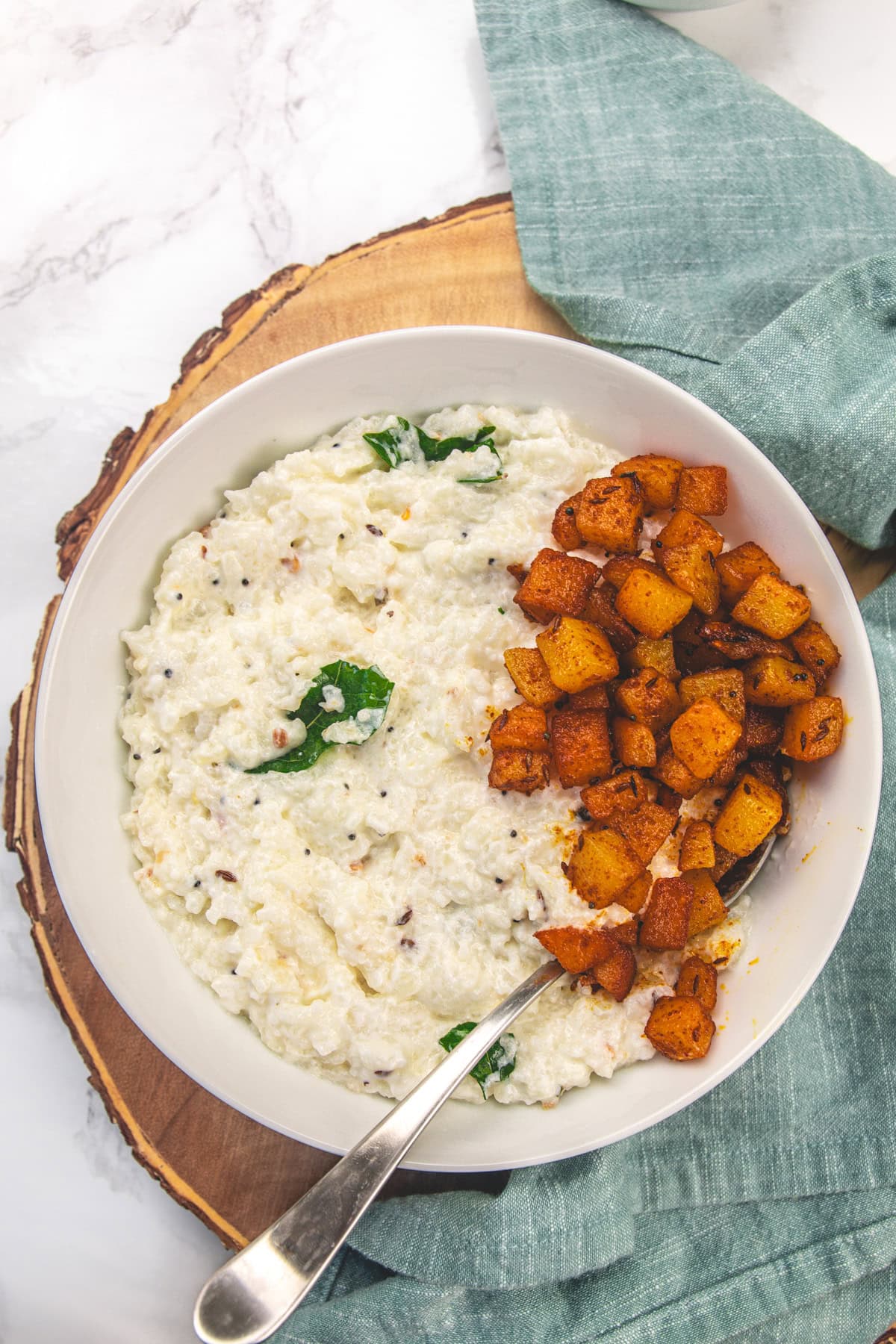 Curd rice and potatoes in a bowl with spoon.
