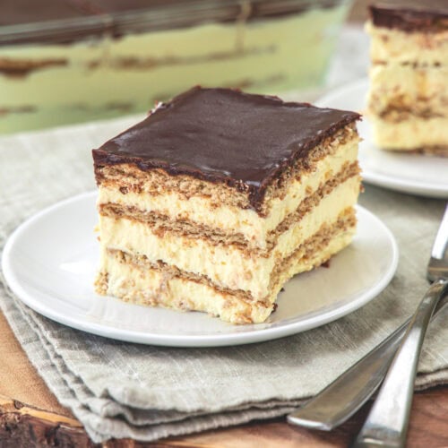 A square piece of Chocolate Eclair Cake in a plate with another plate and pan in the back.