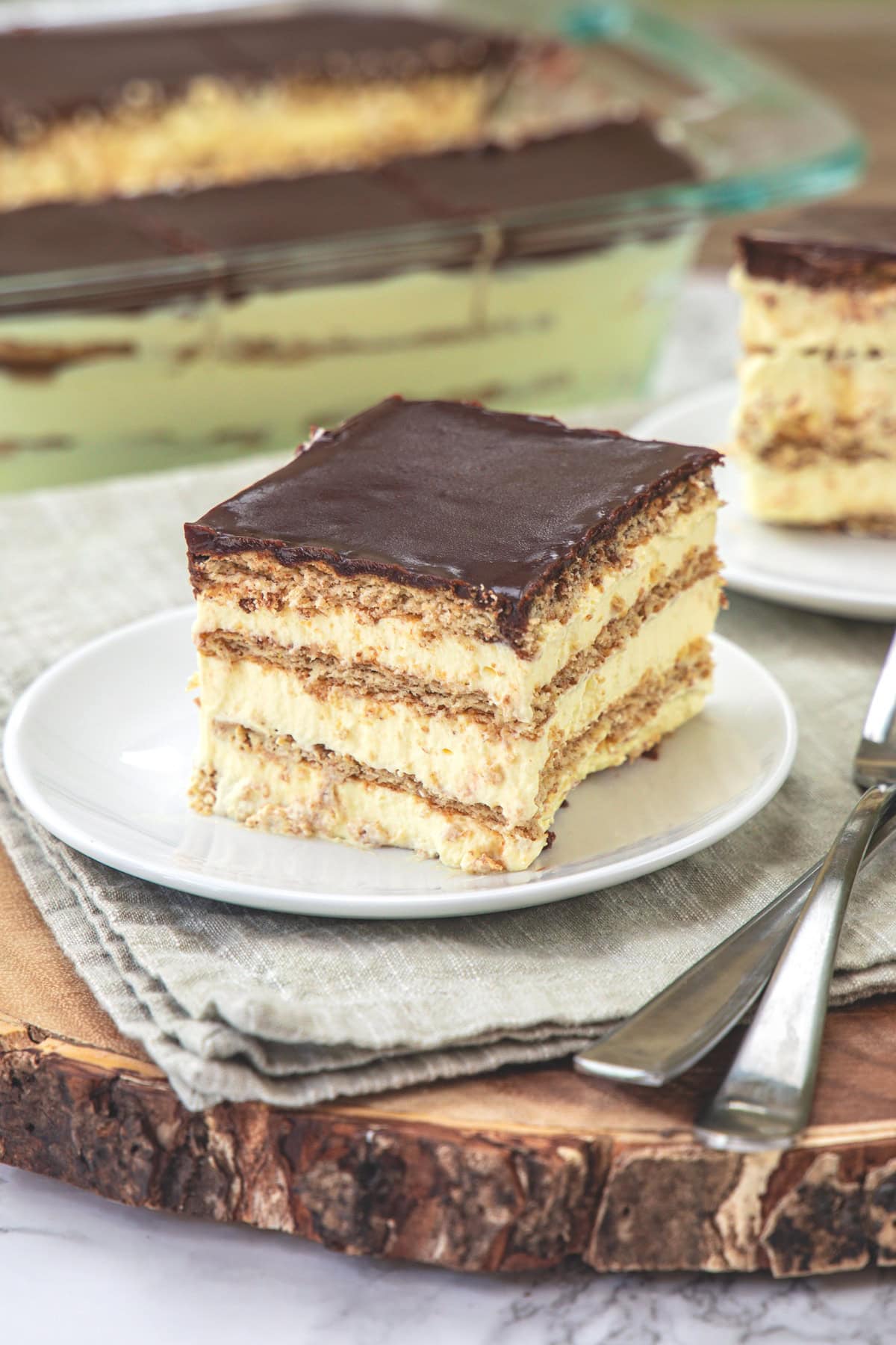 A square piece of Chocolate Eclair Cake in a plate with another plate and pan in the back.