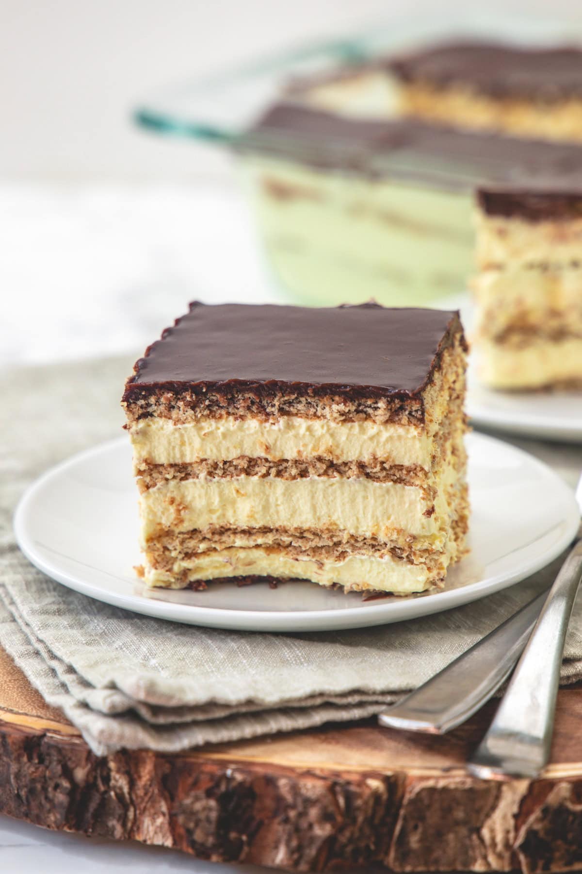 A piece of chocolate eclair cake in a plate with rest cake in the back.