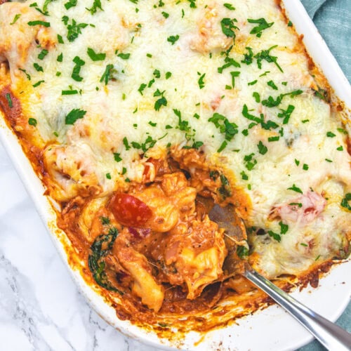Taking a ladle full of baked tortellini from the casserole.
