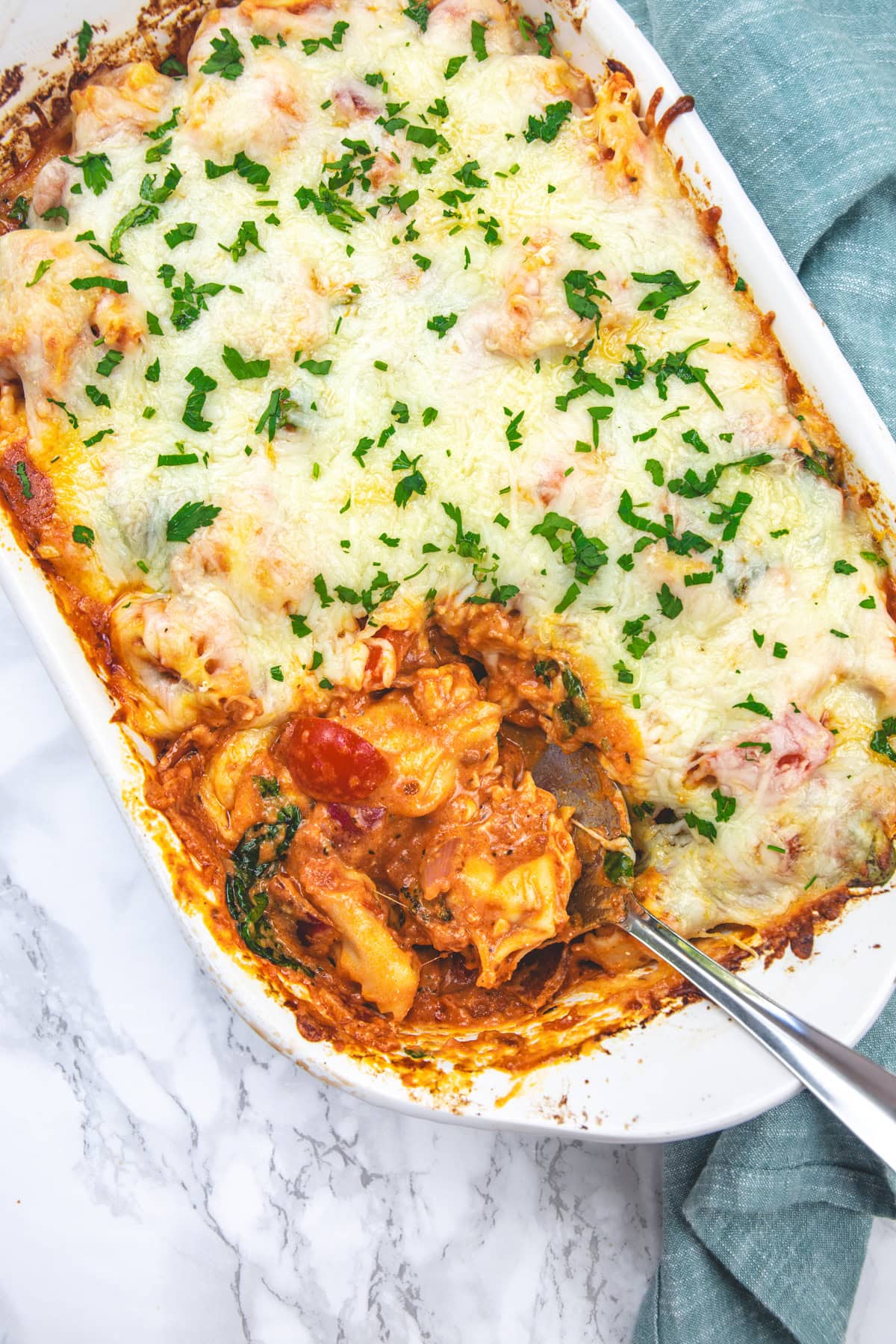 Taking a ladle full of baked tortellini from the casserole.