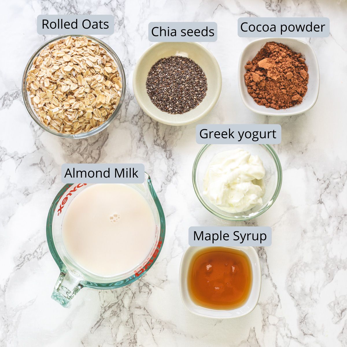 Chocolate overnight oats ingredients in bowls and cup with labels.