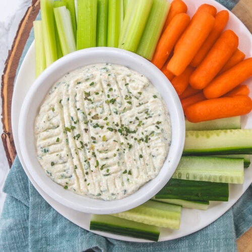 Cottage cheese dip in a bowl with carrots, cucumber and celery in a plate.