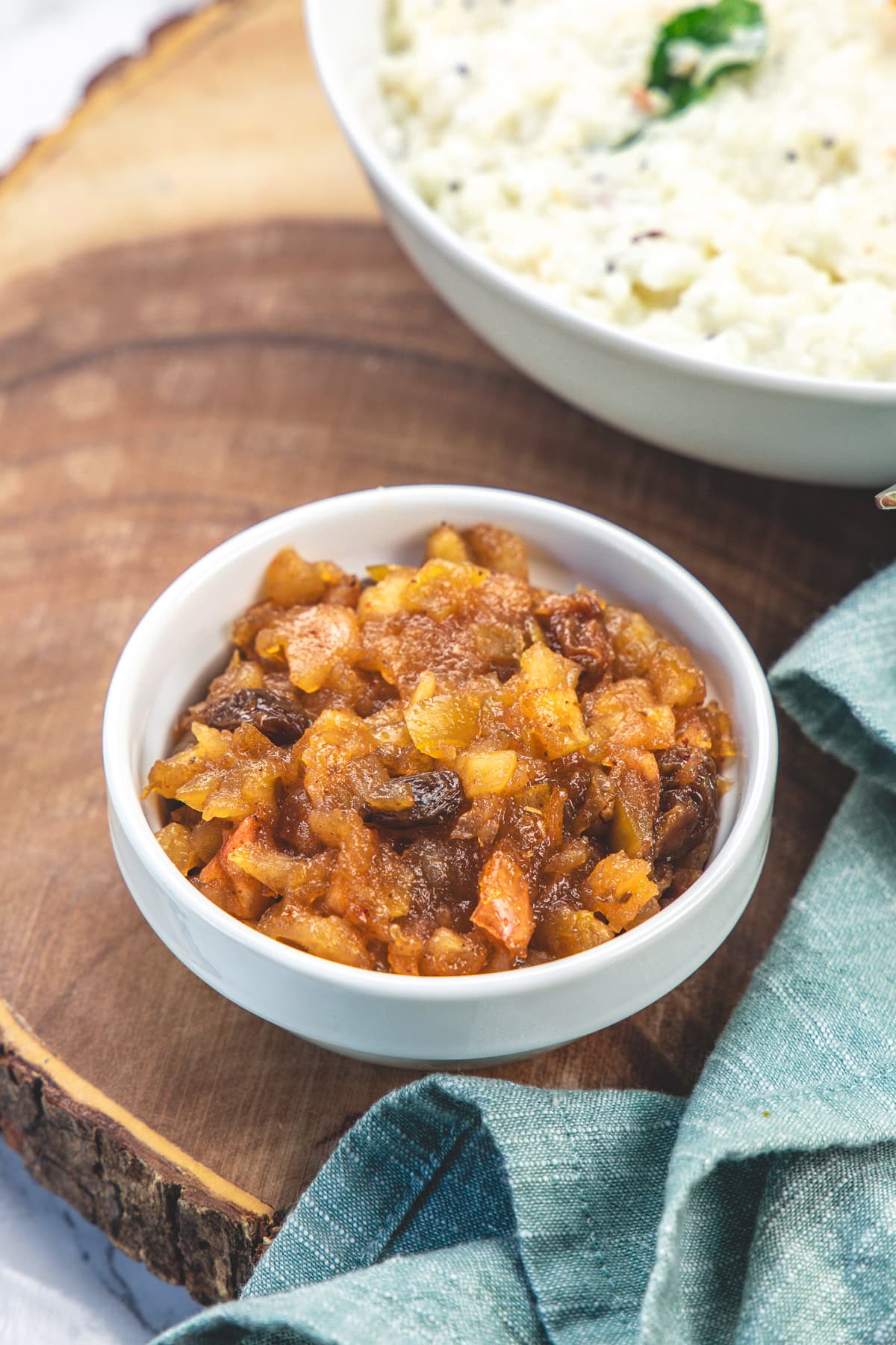 A small bowl of apple chutney with curd rice in the back.