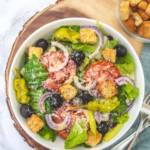 Olive garden salad served in a large bowl with a small bowl of croutons in the back.