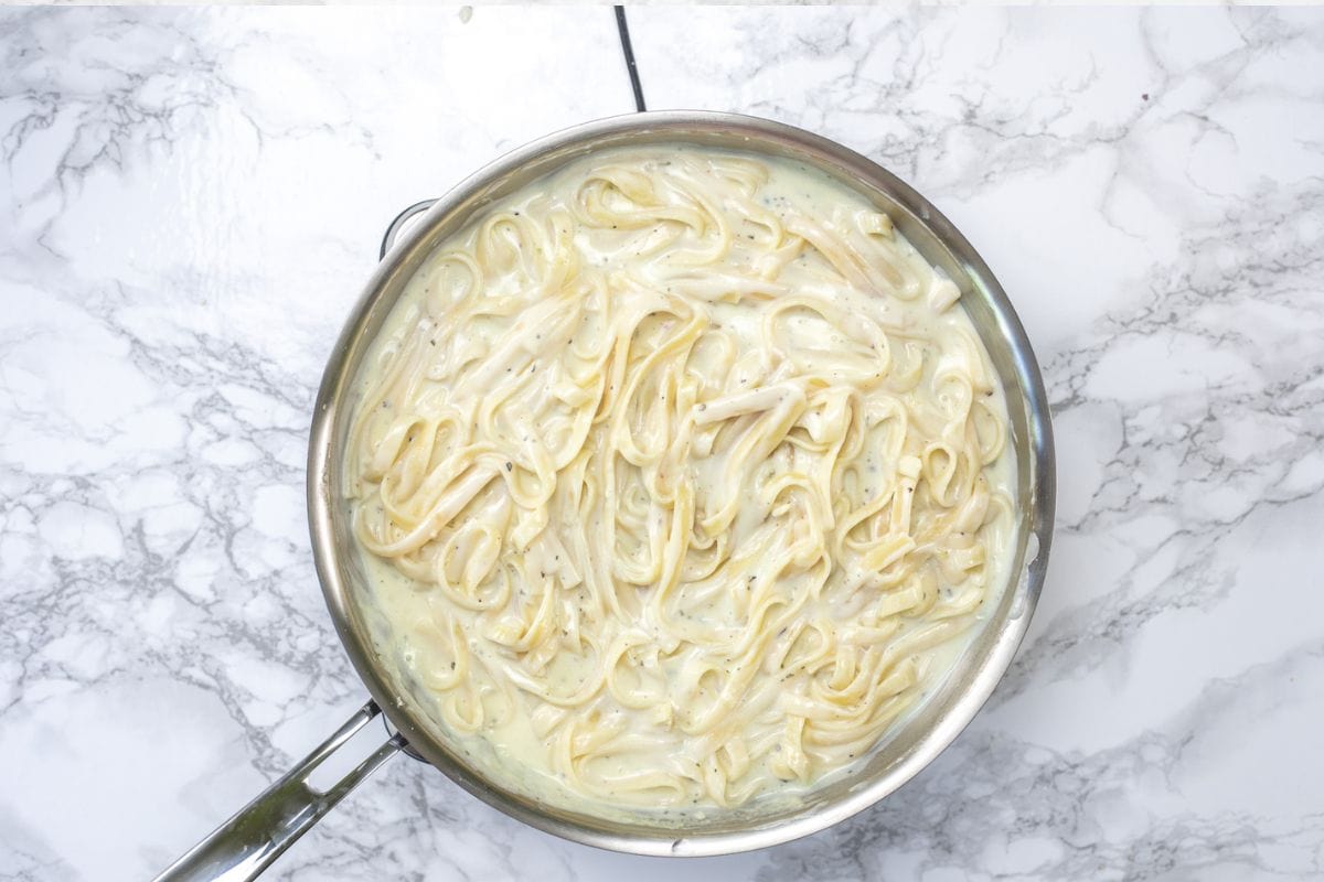 Adding cooked fettuccine pasta in Olive Garden Copycat Alfredo sauce.