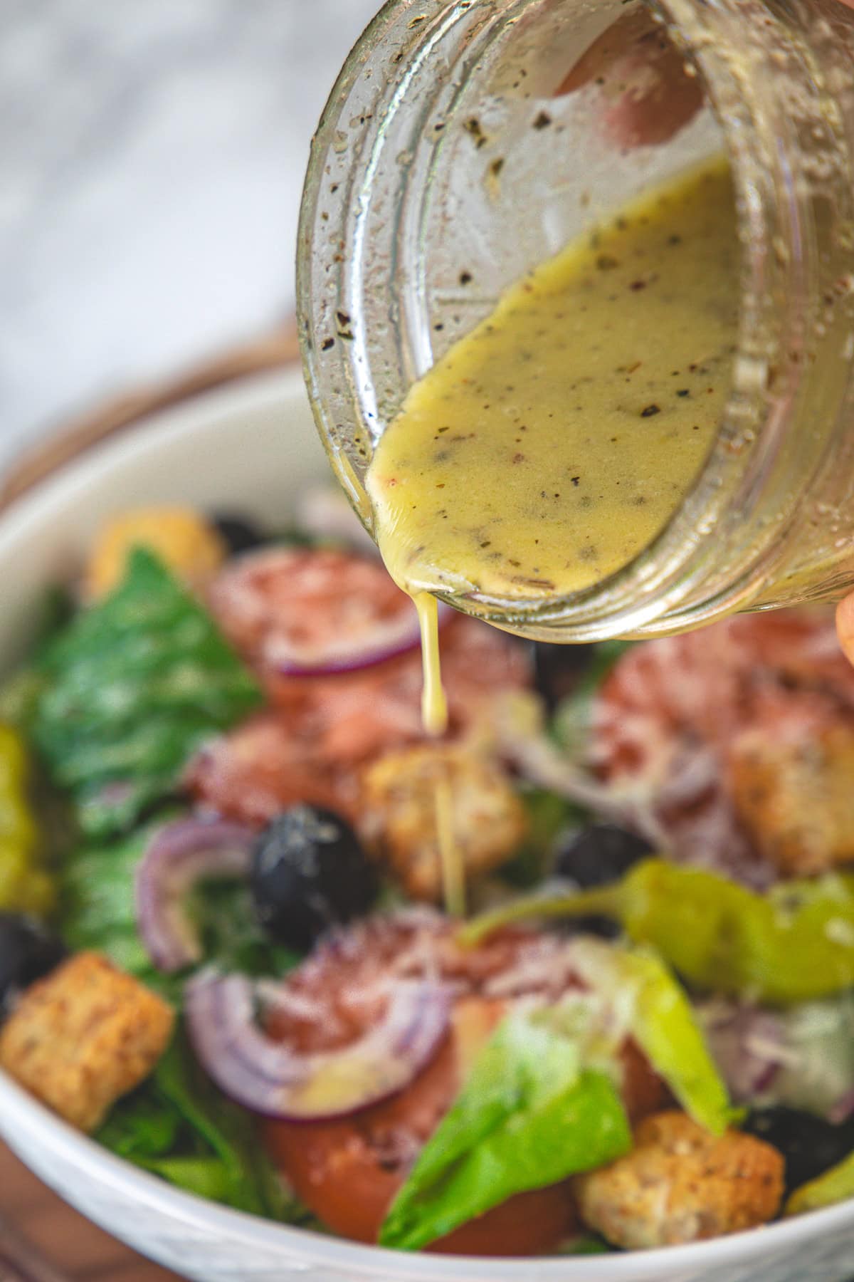 Pouring olive garden salad dressing in a salad bowl.