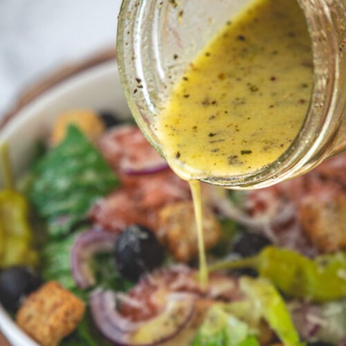 Pouring copycat olive garden salad dressing in a salad bowl.