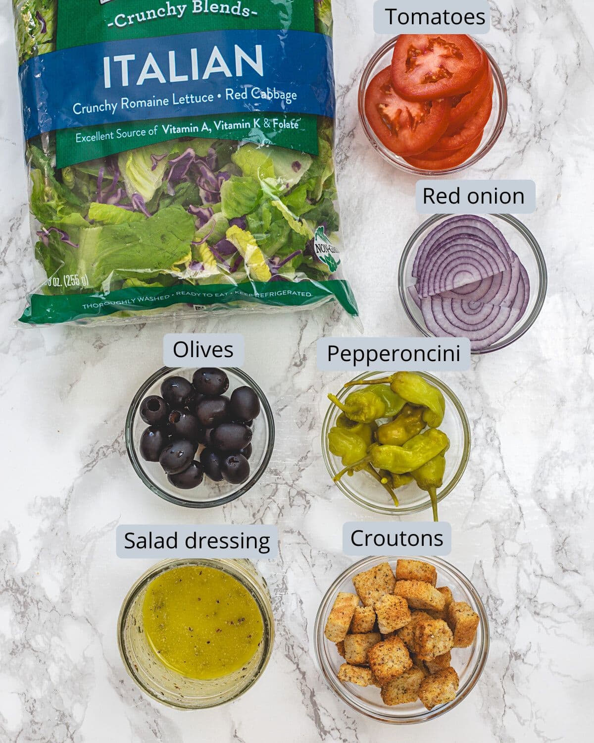 Copycat Olive Garden salad ingredients in bowls with labels.