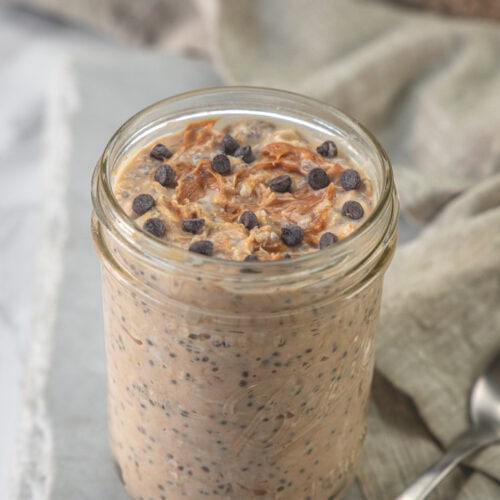 A jar of peanut butter overnight oats garnished with peanut butter and chocolate chips.